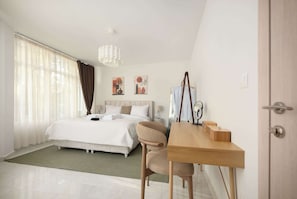 Quarto de hotel com uma cama, uma escrivaninha, uma cadeira, uma luminária e obras de arte na parede.