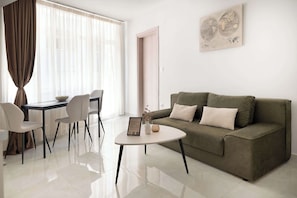 Uma sala de estar moderna com um sofá, uma mesa de centro redonda e uma área de jantar com cadeiras e mesa.