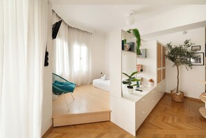 A modern, well-lit room with a bed, a chair, a desk, and a mirror. - Estia Premium Apartments - Capri Blue Salonica (Thessaloniki)