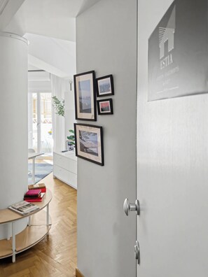 A hallway with a white door, a small table with books, and framed pictures on the wall. - Estia Premium Apartments - Capri Blue Salonica (Thessaloniki)