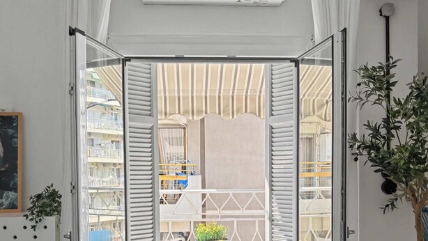 Ein Zimmer mit einer Schiebetür zum Außenbereich, der einen Tisch und Stühle, ein blaues Sofa, eine Pflanze und einen Deckenventilator bietet.
