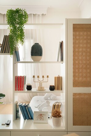 A neatly organized room with a bed, a shelf with books, a decorative vase, and a plant. - Estia Premium Apartments - Capri Blue Salonica (Thessaloniki)