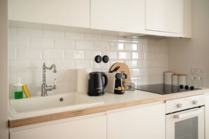 A kitchen with white cabinets, a stainless steel faucet, a coffee maker, and a kettle. - Estia Premium Apartments - Capri Blue Salonica (Thessaloniki)