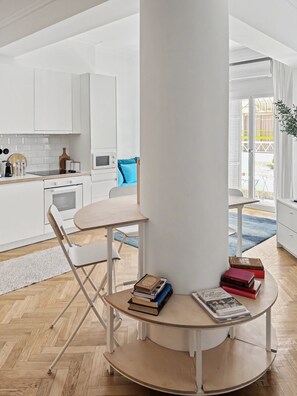 A modern kitchen with white cabinetry, a central island with books, and a view to the outside. - Estia Premium Apartments - Capri Blue Salonica (Thessaloniki)
