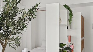 Ein schlicht eingerichtetes Schlafzimmer mit einem Bett, einem weißen Kleiderschrank, einem kleinen Tisch und einem Topf mit Pflanze.