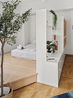 A minimalist bedroom with a bed, a white wardrobe, a small table, and a potted plant. - Estia Premium Apartments - Capri Blue Salonica (Thessaloniki)