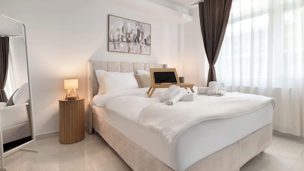 A modern hotel room with a large bed, a bedside table with a lamp, a tablet, and neatly folded towels. - Estia Premium Apartments - Superior Suite Vackhou 1 #1.2 (Thessaloniki)