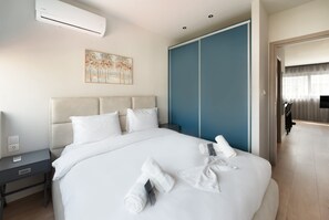 A hotel room with a bed, a nightstand, a wall-mounted air conditioner, a painting, a wardrobe, and a television in the adjacent room. - Estia Premium Apartments - Valouritou 52 Sqm2 Apartment (Thessaloniki)