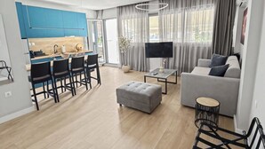 Un salon moderne avec un canapé gris, un petit pouf, un téléviseur et un coin repas comprenant des chaises et une table.