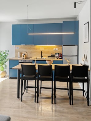 A modern kitchen with blue cabinets, a wooden countertop, and a dining area with four chairs. - Estia Premium Apartments  - Valouritou 25 Big Balcony (Thessaloniki)