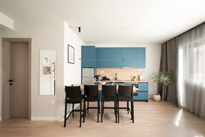A modern kitchen with blue cabinets, a dining table with chairs, and a potted plant. - Estia Premium Apartments  - Valouritou 25 Big Balcony (Thessaloniki)