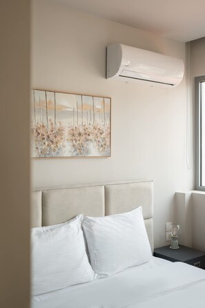 Ein Hotelzimmer mit einem Bett, einer Wandklimaanlage, einem gerahmten Kunstwerk und einem Nachttisch mit Lampe.