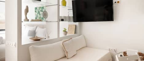 Una sala de estar moderna con un sofá blanco, un televisor montado en la pared y un comedor con mesa y sillas blancas.