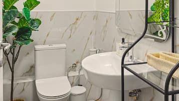 A bathroom with a toilet, sink, and mirror, with two wreaths on the wall and a plant on the left.