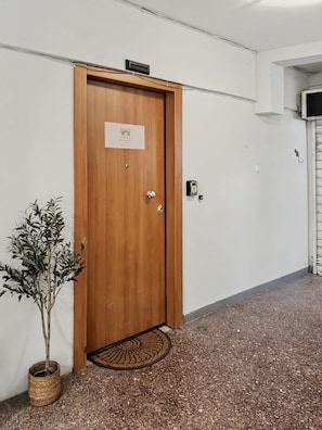 Una porta in legno con un cartello, una pianta in vaso e un tappetino.