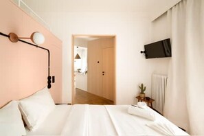 Une chambre à coucher avec un lit, un téléviseur fixé au mur et une porte donnant sur une autre pièce.
