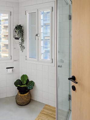 Une salle de bain avec des murs carrelés de carreaux blancs, une porte en bois, une cabine de douche en verre et une plante en pot.