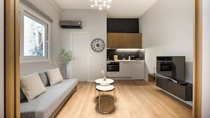 A modern living space with a sofa, a small round table, a kitchen area, and a TV.