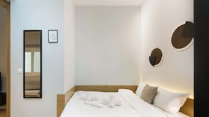 A neatly made bed with white linens, a wooden headboard, and a wall-mounted mirror.