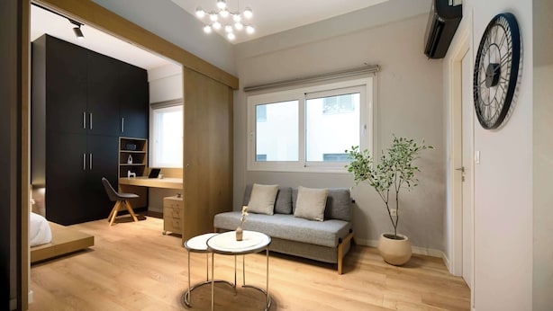 A modern living room with a sofa, two round tables, a potted plant, a large clock, and a wardrobe.