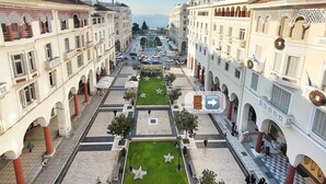 A courtyard with a central lawn, surrounding buildings with balconies, and a view of the sea.