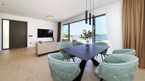 Uma sala de estar moderna com sofá, televisão, mesa de jantar com cadeiras e uma grande janela com vista.