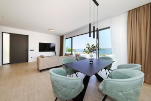 Ein modernes Wohnzimmer mit Sofa, Fernseher, Esstisch mit Stühlen und einem großen Fenster mit Aussicht.