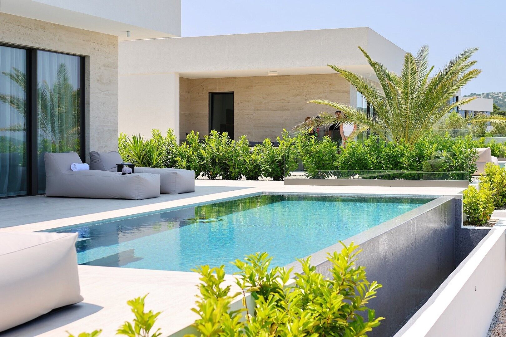 A modern outdoor pool area with a minimalist design, including a seating area with cushions and a clear view of the pool.