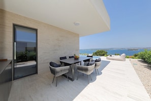 A modern outdoor dining area with a table and chairs, a glass door, and a view of the sea. - Villa D7 with private pool 1 km from sea (Tkon)