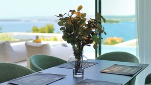 Una mesa con vistas despejadas al mar, un florero de vidrio con follaje y un menú sobre la mesa.