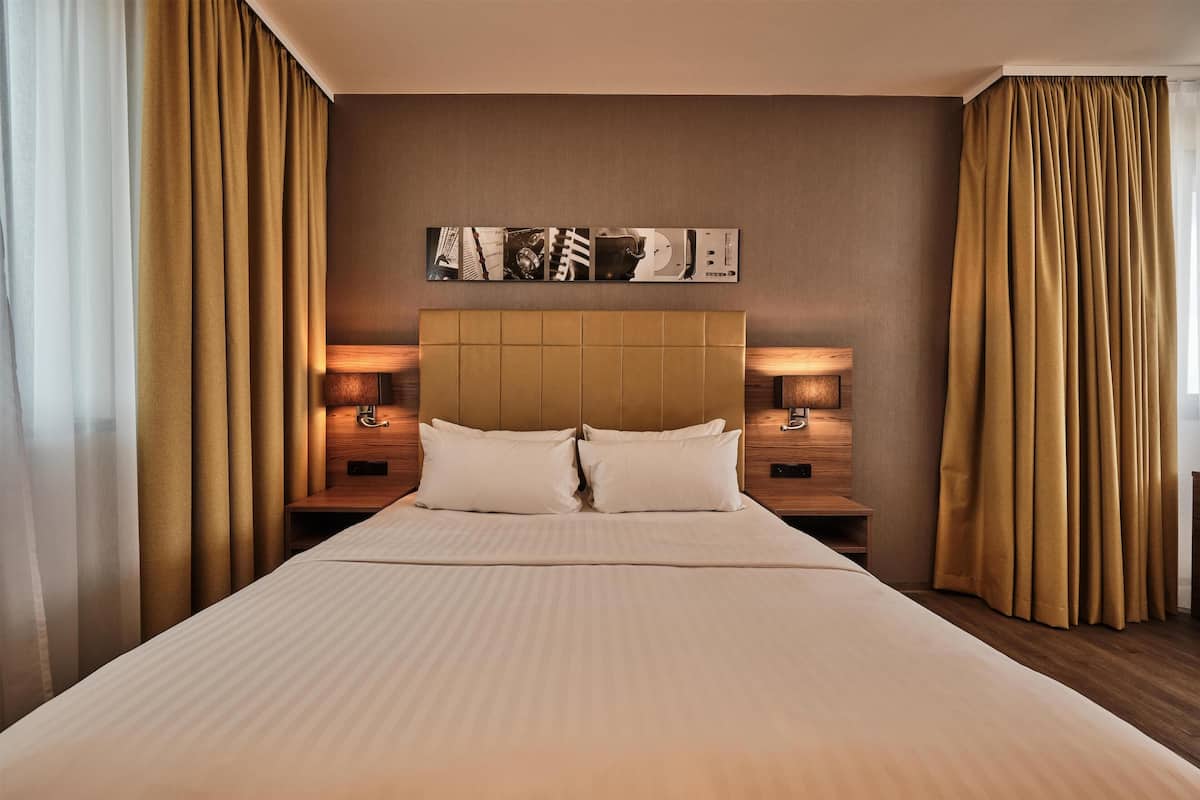 A hotel room with a large bed, two bedside tables with lamps, a headboard, and a wall-mounted artwork.