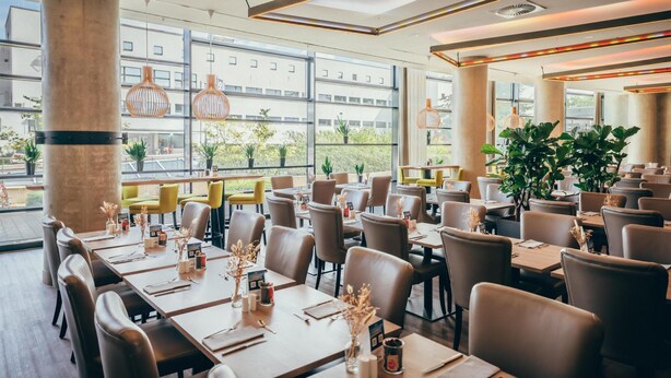 A restaurant with tables set for dining, large windows, and indoor plants. - Radisson Blu Hotel, Bonn (T) (Bonn)