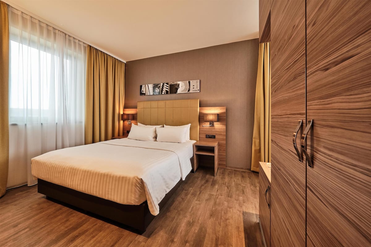 A hotel room with a large bed, wooden wardrobe, bedside lamps, and a wall-mounted artwork.