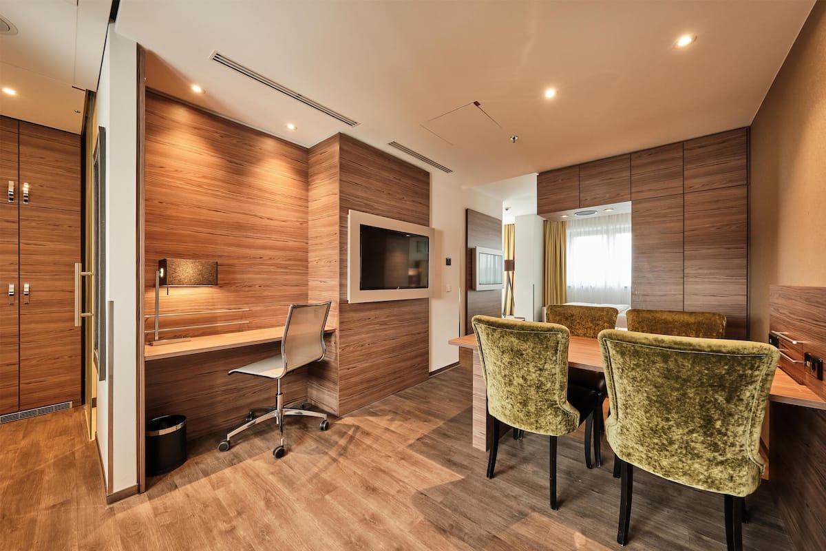 A modern office with a wooden panel wall, a mounted TV, a desk with a chair, and a dining area with chairs.