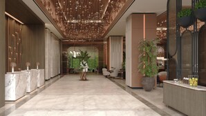 Un hall d’hôtel moderne avec un comptoir de réception en marbre, une grande plante en pot et un luminaire décoratif au plafond.