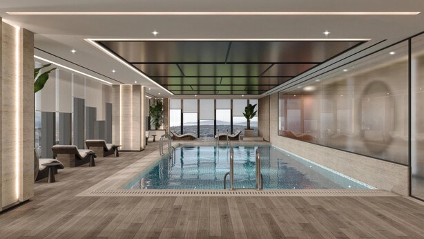Une piscine intérieure moderne, dotée de chaises longues, offrant une vue sur la ville et un plafond haut avec des luminaires encastrés.