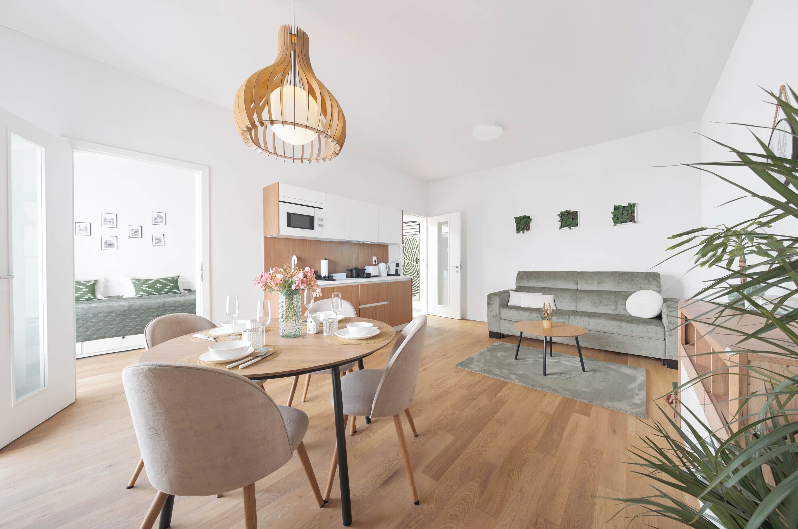 Un salon moderne comprenant un coin repas, un canapé gris, une table à manger en bois et un luminaire suspendu.