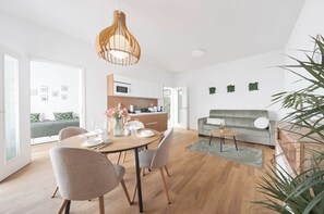 A modern living room with a dining area, a grey sofa, a wooden dining table, and a hanging light fixture. - Kajetanka Residence - with terrace and free parking on weekends (Hlavní město Praha)