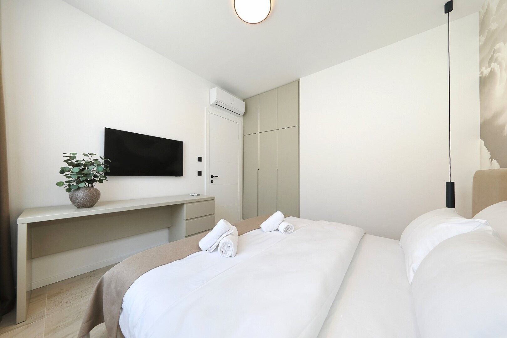 A modern hotel room with a bed, a desk, a TV, and a wardrobe.