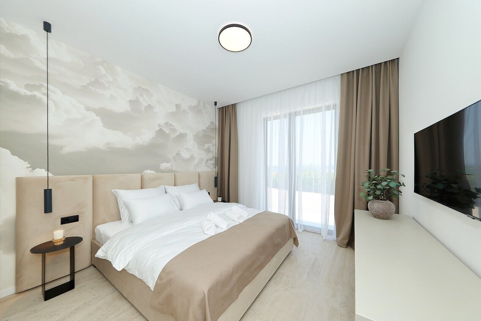Ein modernes Hotelzimmer mit einem großen Bett, einem Flachbildfernseher, einem an der Wand befestigten Fernseher, einer Deckenleuchte und einem großen Fenster mit Vorhängen.