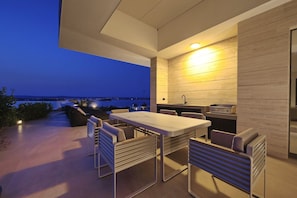 Un área de comedor al aire libre con mesa y sillas, una cocina integrada y vista al mar.