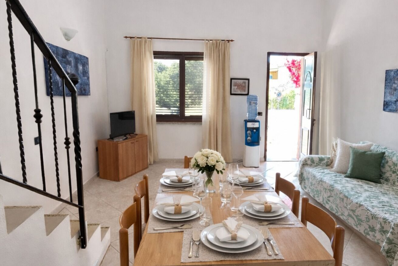 A dining area with a table set for four, a sofa, a staircase, and a water dispenser.