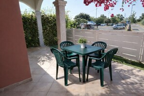 An outdoor patio with a table and chairs, a potted plant, and a view of a street with parked cars. - ANFITEATRO 39 - BUDONI SWEET HOME (Porto Ottiolu)
