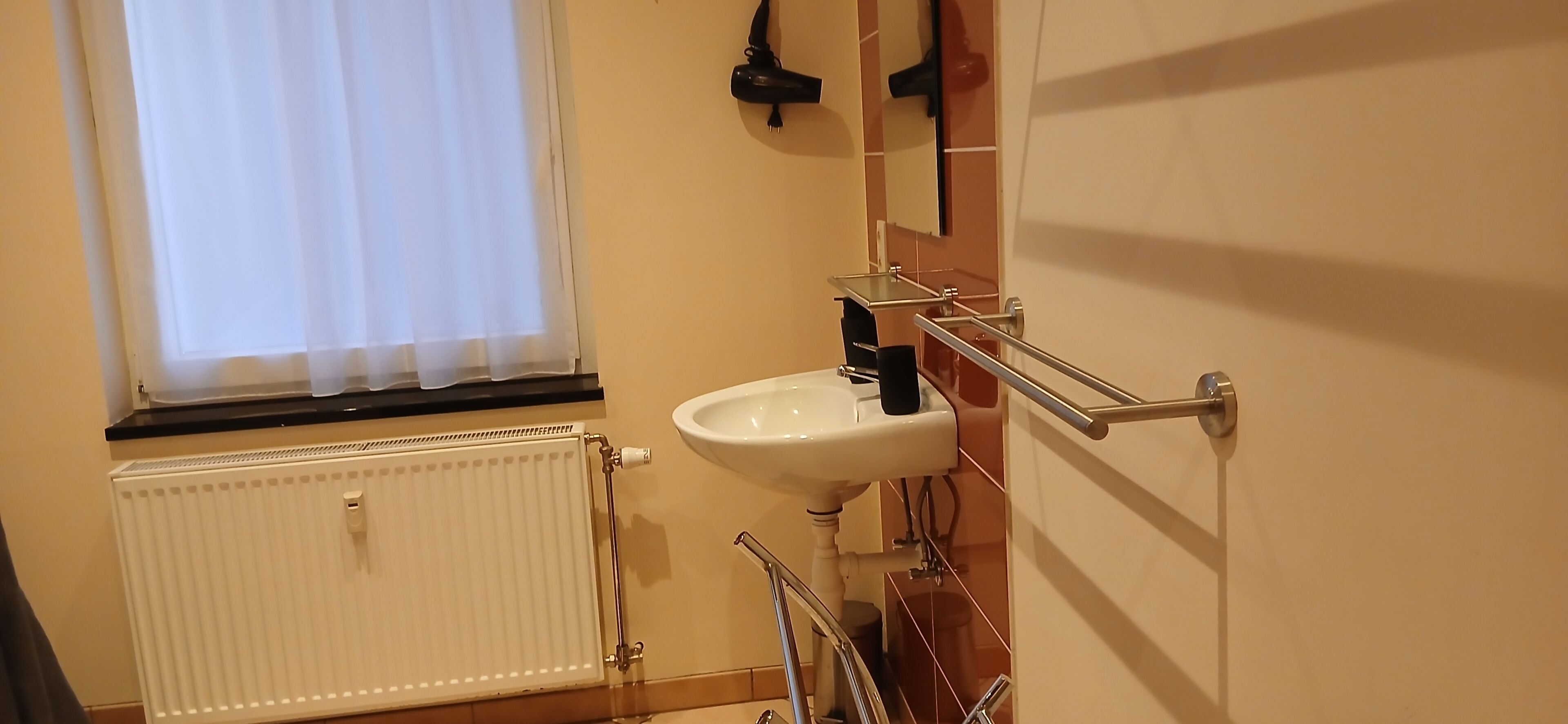 Een badkamer met een wit wastafelmeubel, een handdoekhouder, een radiator en een raam met gordijnen.