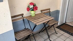 A small outdoor table with a green vase of flowers, a wooden bench, and a door in the background.