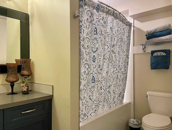 A bathroom with a patterned shower curtain, a toilet, a sink with decorative vases, and a towel rack.