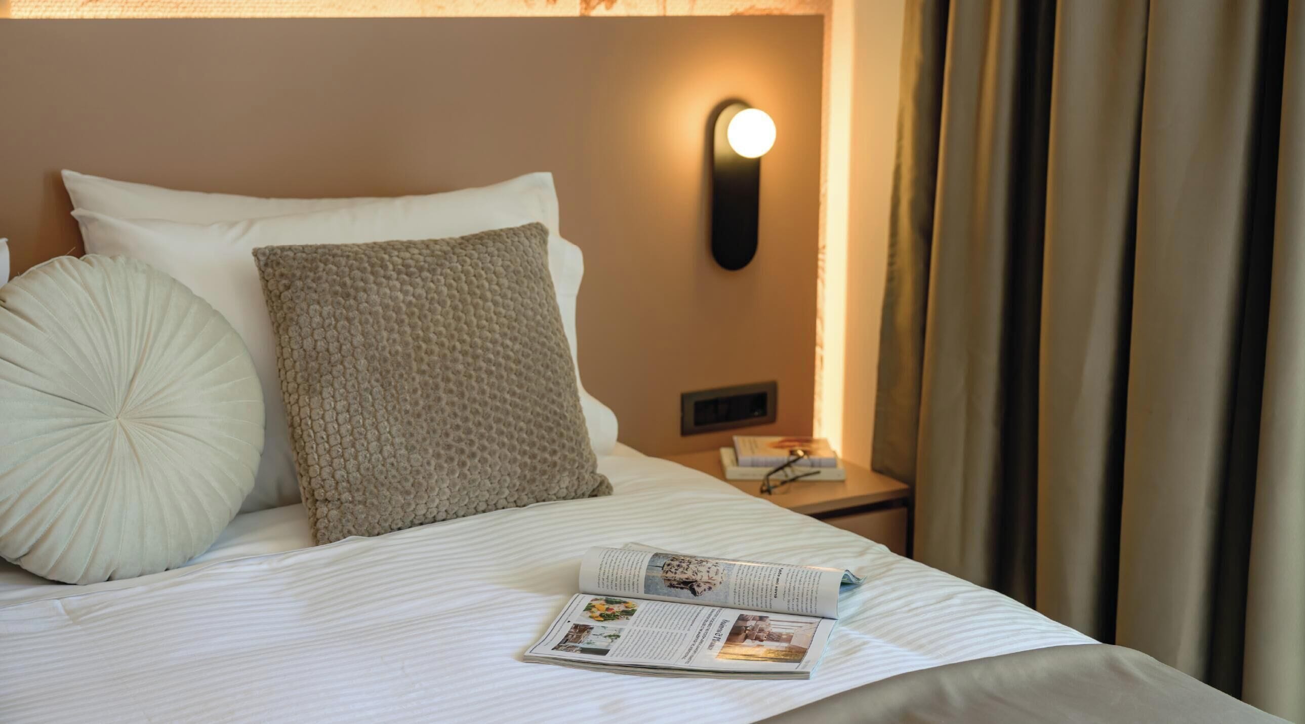 Een net opgemaakt bed met een kussen, een bedlampje en een boek op het nachtkastje.