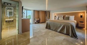 Quarto de hotel moderno com uma cama grande, banheiro com toucador e vista para o exterior.