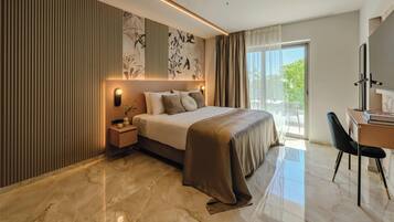 A modern hotel room with a bed, bedside table, lamp, and a desk with a chair.
