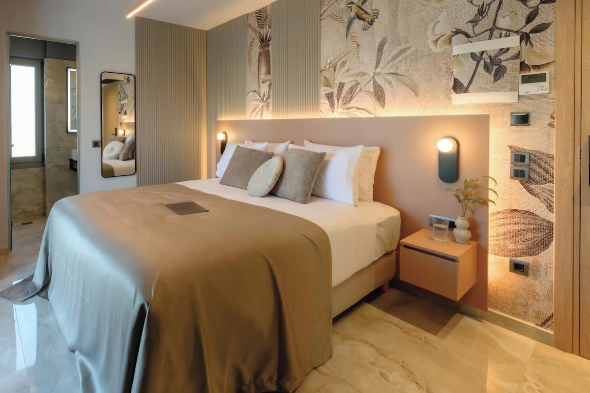 A modern hotel room with a large bed, a bedside table with a vase, a mirror, and a wall with a tropical mural.